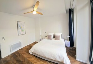 Un dormitori amb llit, ventilador al sostre, mapa a la paret i una tauleta de nit amb làmpada.