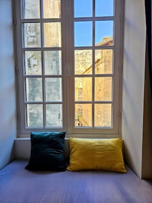 A room with a bed against a wall, a window with a view of old buildings, and a pillow on the bed. - Chemin du muguet T2 hyper centre (Bordeaux)