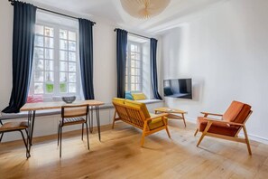 A modern living room with a wooden floor, a dining table with chairs, a sofa, and a TV mounted on the wall. - Chemin du muguet T2 hyper centre (Bordeaux)