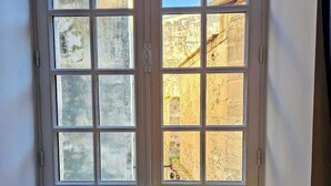 Ein Zimmer mit einem Bett an der Wand, einem Fenster mit Blick auf alte Gebäude und zwei Kissen auf dem Bett.