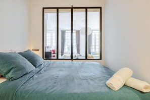 A bedroom with a bed, pillows, a window, and a view of the outside. - Chemin du muguet T2 hyper centre (Bordeaux)