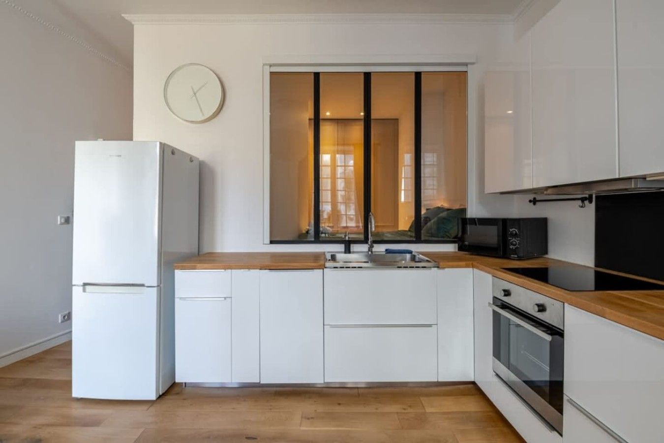 Una cocina compacta con armarios blancos, encimera de madera, horno integrado y microondas.