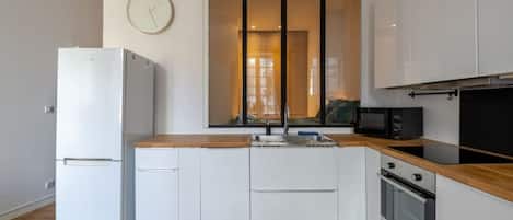 Una cocina compacta con armarios blancos, encimera de madera, horno integrado y microondas.