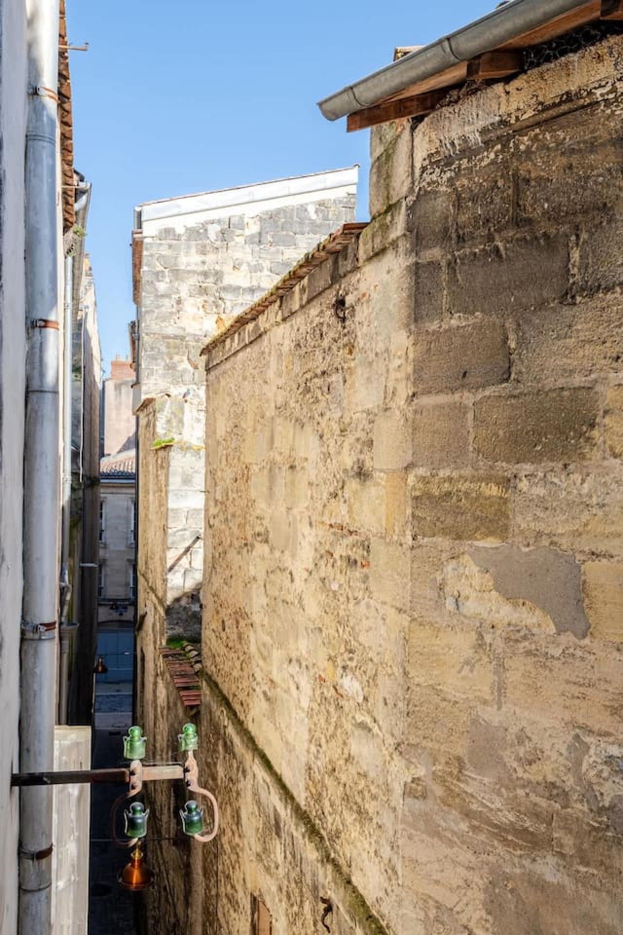 A narrow alleyway with stone walls and a metal pipe on the left.