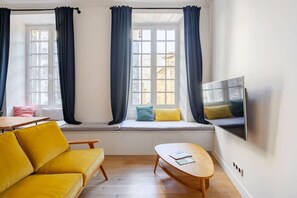 A modern living room with a sofa, a small table, and a TV mounted on the wall. - Chemin du muguet T2 hyper centre (Bordeaux)
