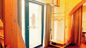 Une pièce avec une porte en bois, un porte-manteau et une fenêtre avec des rideaux.