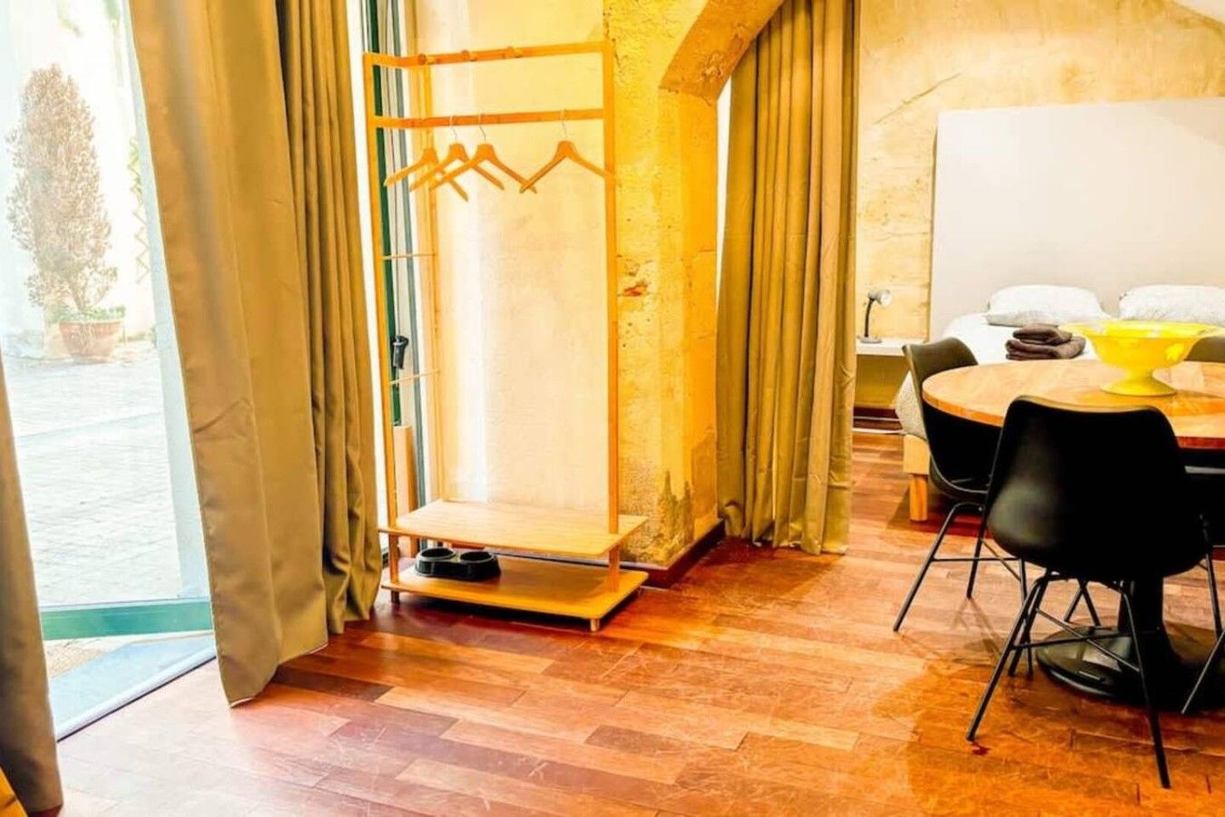 A room with a wooden floor, a table with chairs, a yellow bowl, and a window with curtains.
