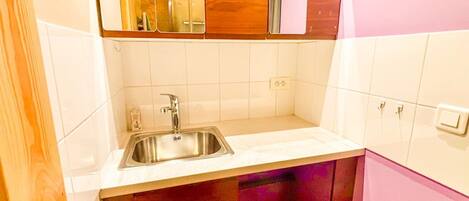 A kitchen with a stainless steel sink, white tiled walls, wooden cabinets, and a pink refrigerator.