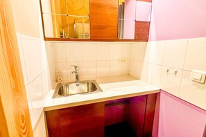 Eine Küche mit einer Edelstahlspüle, weißen Fliesenwänden, Holzschränken und einem rosa Kühlschrank.