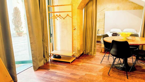 Une pièce avec un plancher en bois, une table à manger avec des chaises, un tableau blanc et une fenêtre avec des rideaux.