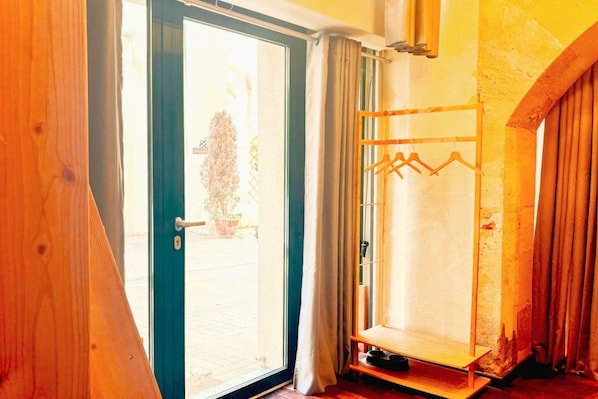 A room with a sliding glass door leading to an outdoor area, a wooden door frame, and a coat rack with hangers. - Charming Mini Loft in the Heart of the Historic Center (Bordeaux)