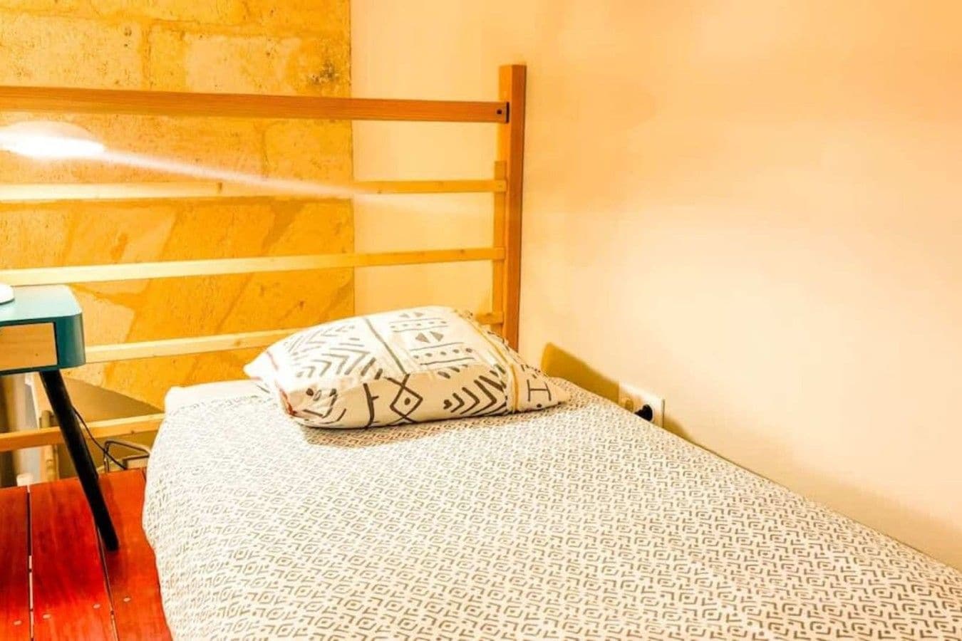 Cama de solteiro com colcha estampada e travesseiro decorativo em quarto com cabeceira de madeira e escrivaninha.
