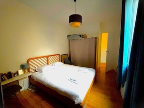 Une chambre à coucher comprenant un lit, un bureau, une chaise, une armoire et un luminaire suspendu.