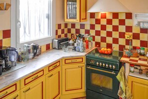 A kitchen with yellow cabinets, a green stove, and a checkered backsplash. - Echoppe Bordelaise typique dans Bordeaux (Bordeaux)