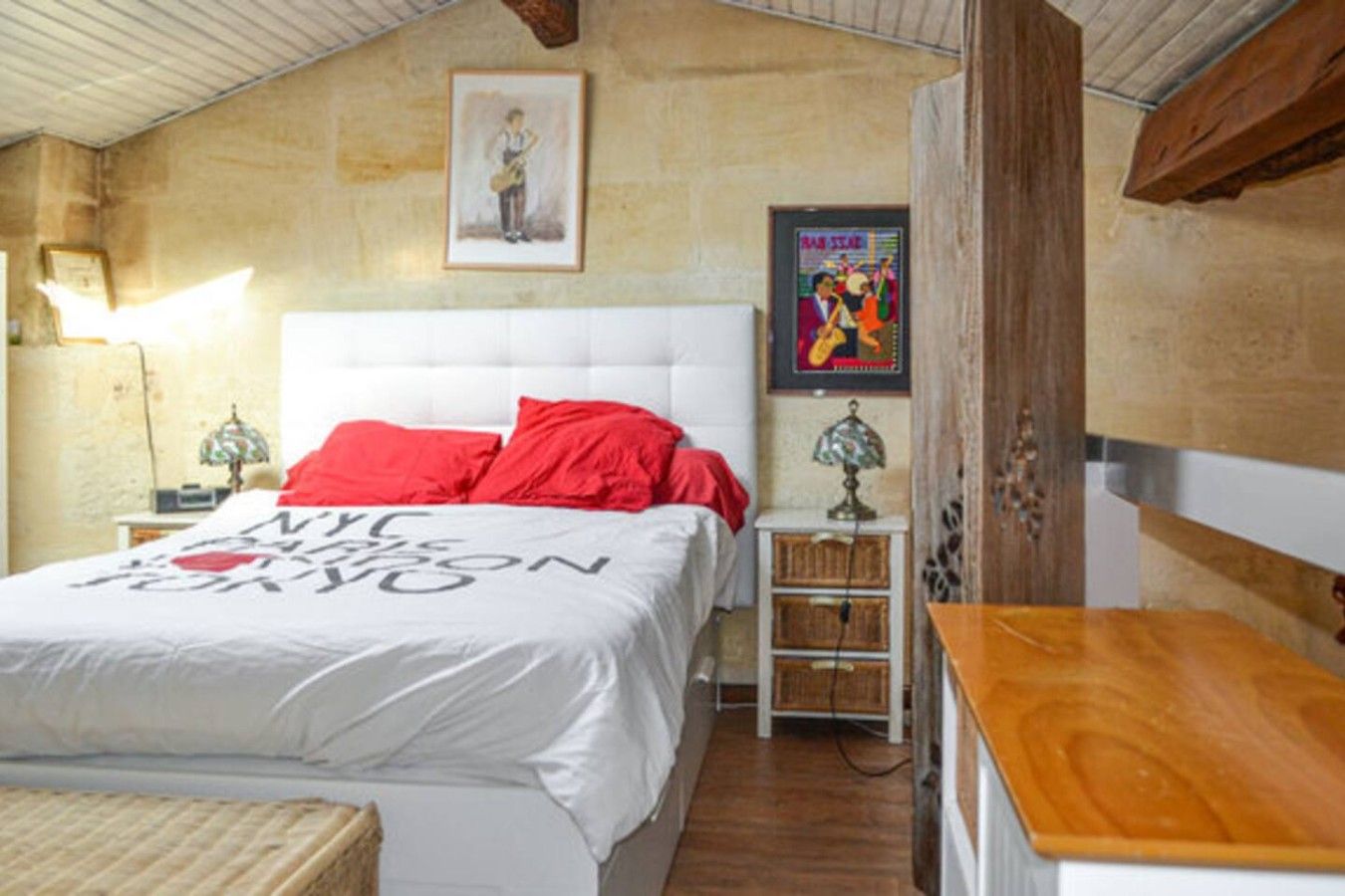 A bedroom with a bed, a nightstand, a lamp, a framed picture on the wall, and a wooden table.