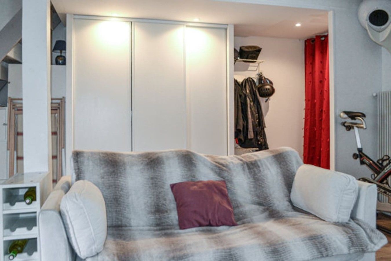 A living room with a sofa, a red curtain, a bicycle, and a closet with hanging clothes.