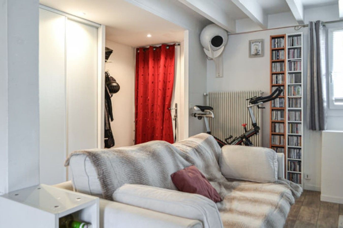 A living room with a sofa, a radiator, a bookshelf, and a bicycle.
