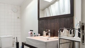 Une salle de bain avec un mur recouvert de carreaux blancs, un grand miroir, un lavabo avec des articles de toilette et un rideau de douche.