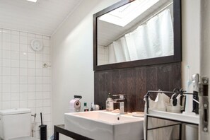 A bathroom with a white tiled wall, a large mirror, a sink with toiletries, and a shower curtain. - Echoppe Bordelaise typique dans Bordeaux (Bordeaux)