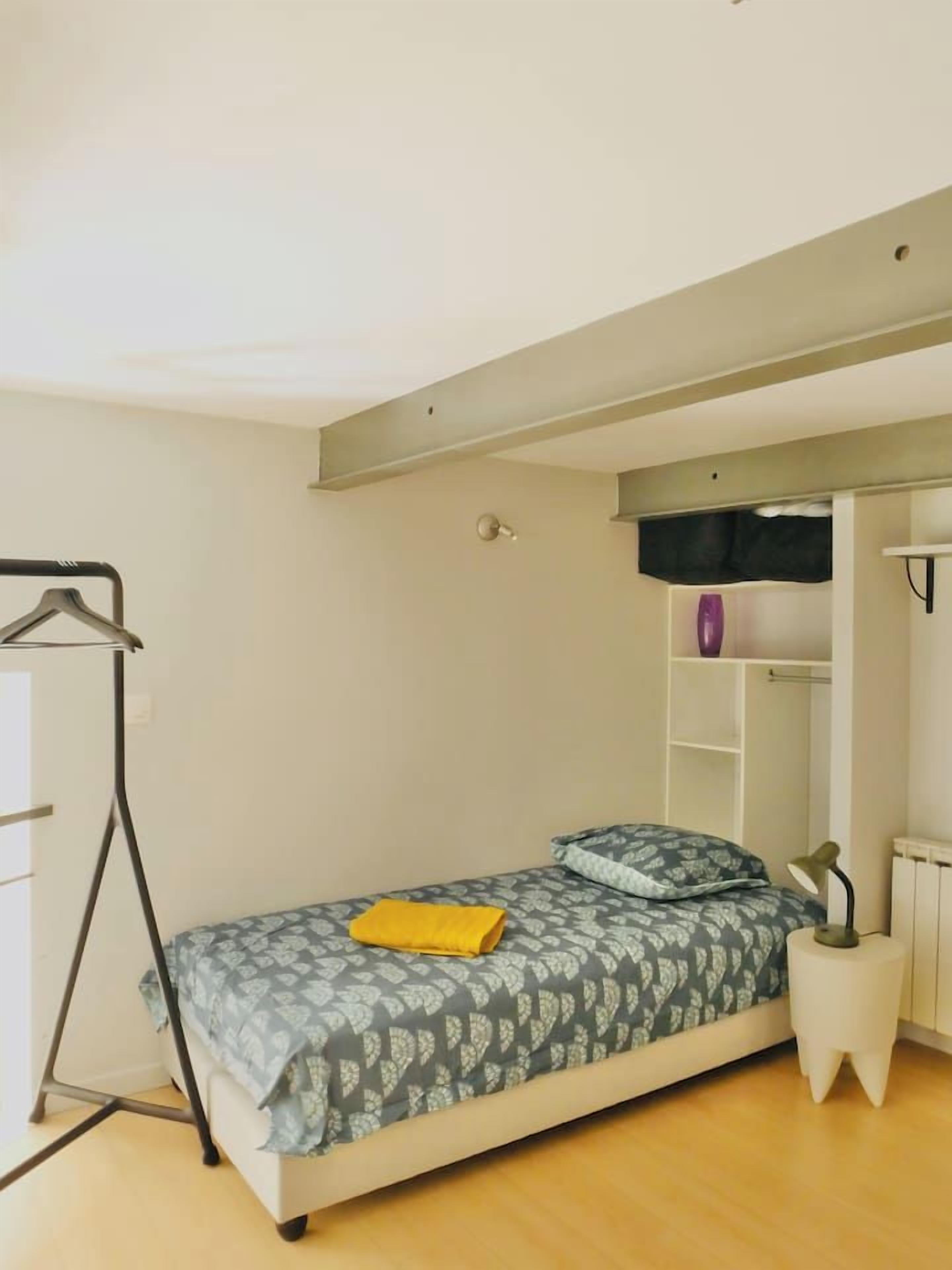 A small, single-bed room with a bed, a bedside table, a hanging clothes rack, and a radiator.