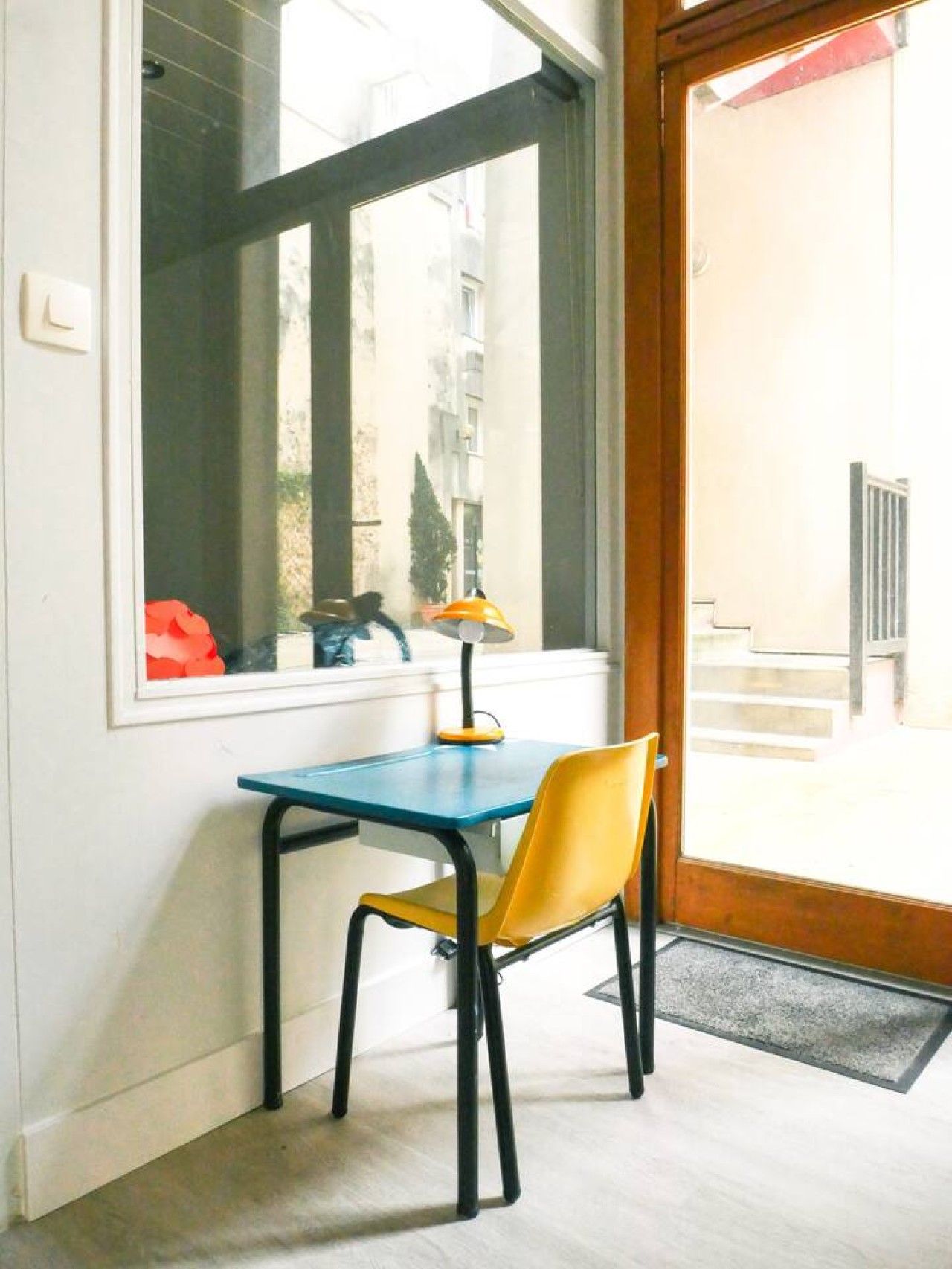 A room with a table and chair, a window with a view of buildings, and a door leading outside.
