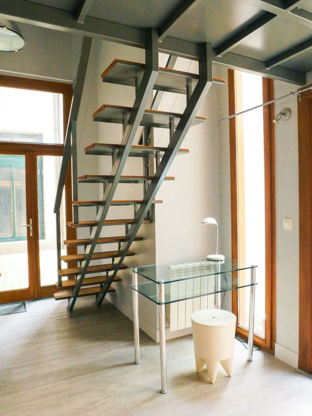 Un intérieur moderne avec un escalier en colimaçon, une table en verre et un tabouret blanc.