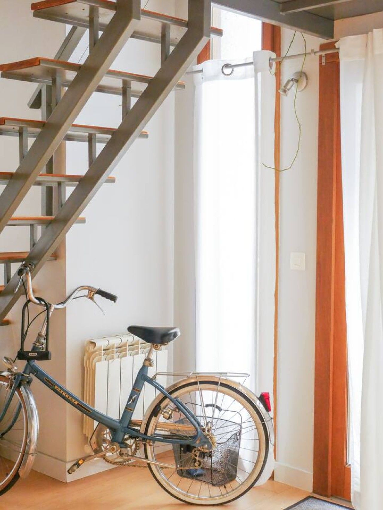 A room with a staircase, a radiator, a bicycle, and a curtain.