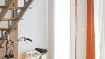 Une pièce avec un escalier, un radiateur, un vélo et un rideau.