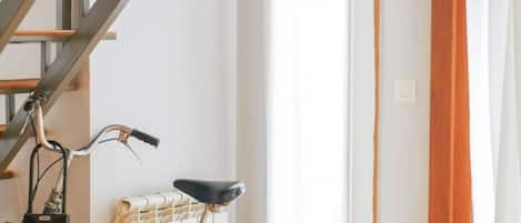 Une pièce avec un escalier, un radiateur, un vélo et un rideau.