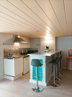Une cuisine moderne avec un îlot central, des tabourets de bar et un luminaire suspendu.