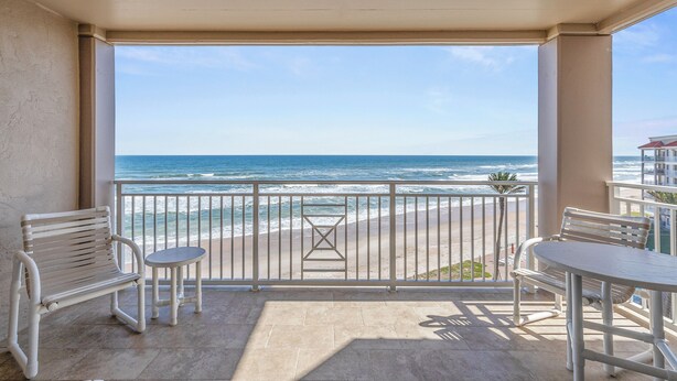 A balcony with a view of the ocean, featuring two white chairs and a small table. - 🌴🌊Beautiful Oceanfront 3BR | Sandpiper 611 | Two Large Pools + Putting Green (New Smyrna Beach)
