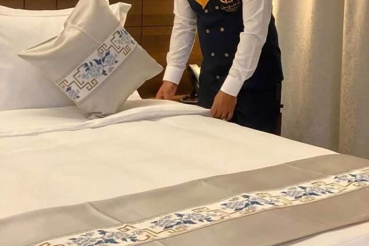 Una habitación de hotel con una cama bien hecha, un cabecero decorativo y un miembro del personal uniformado.
