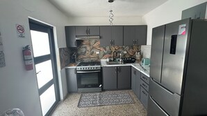 Una cocina compacta con armarios oscuros, una estufa a gas, un microondas y un refrigerador de acero inoxidable.