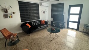 Una sala de estar con un sofá negro, sillones naranjas, una mesa de centro y un ventilador de techo.
