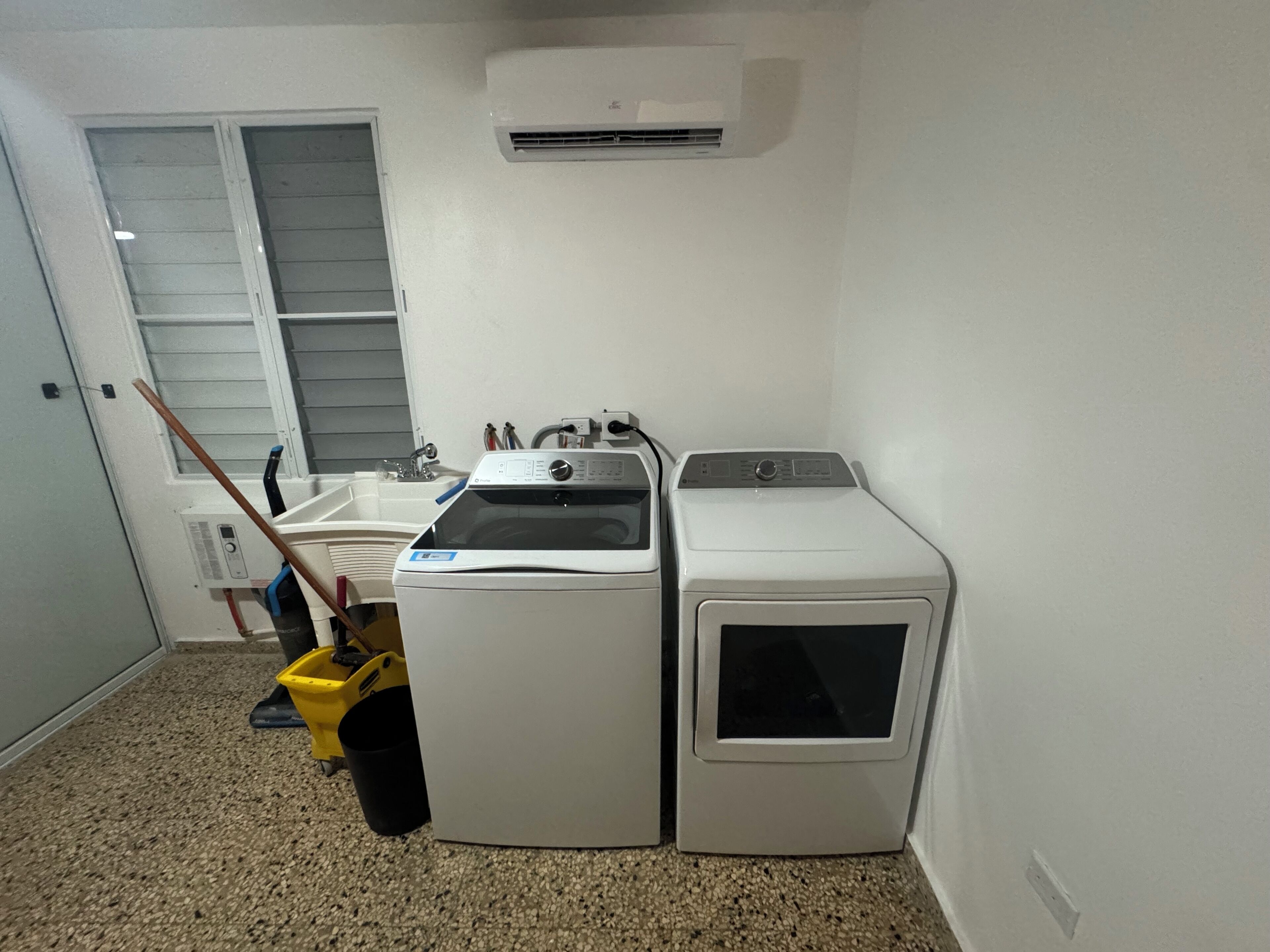 Een wasserette met een wasmachine en droger, een wasbak en een dweil.