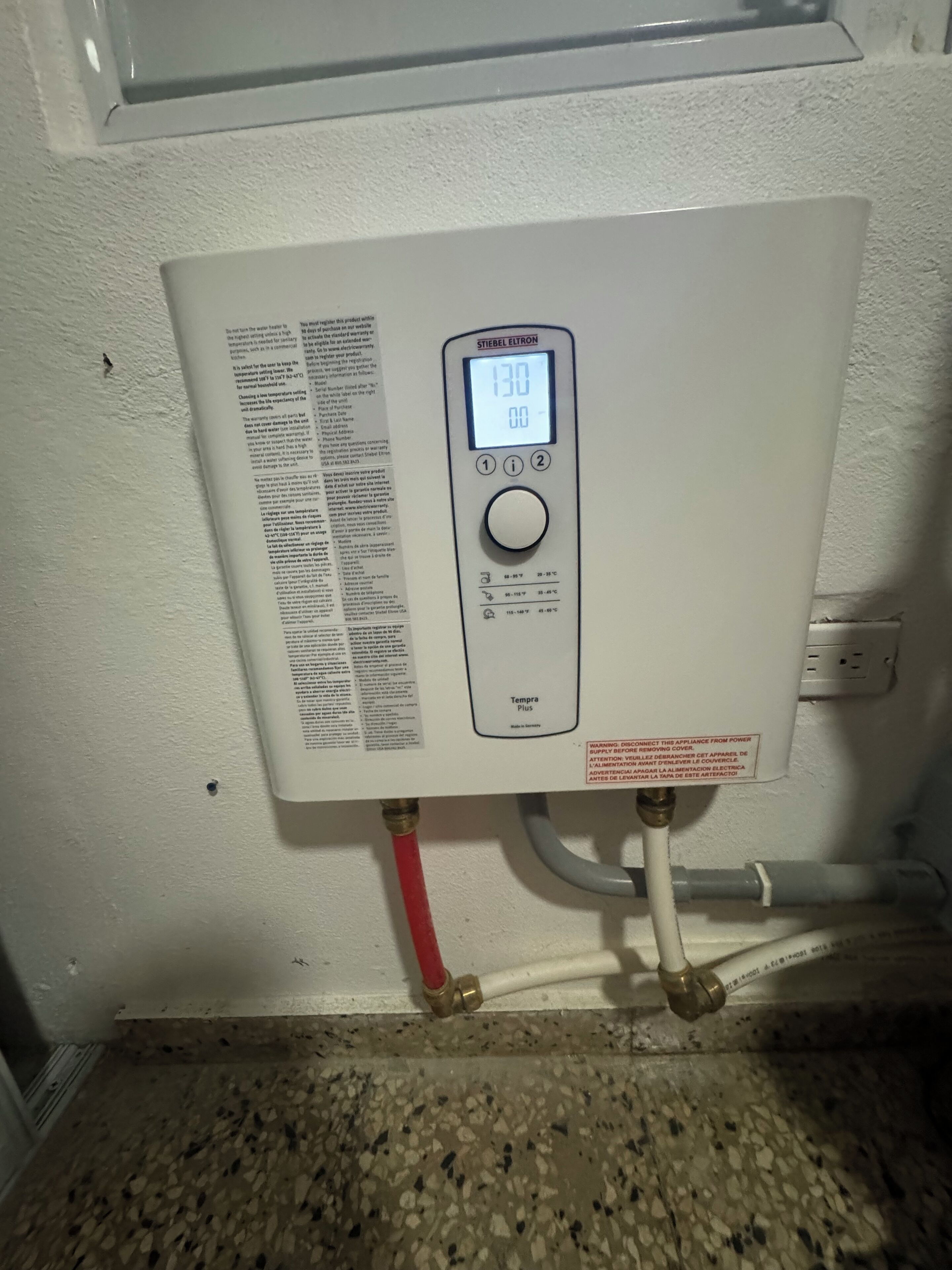 Un termostato blanco con pantalla digital, un manual y una tubería roja y blanca conectada.