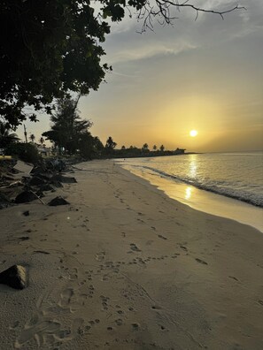 A beach with footprints leading to the water, palm trees, and a sunset. - Suarez Beach House (Río Grande)