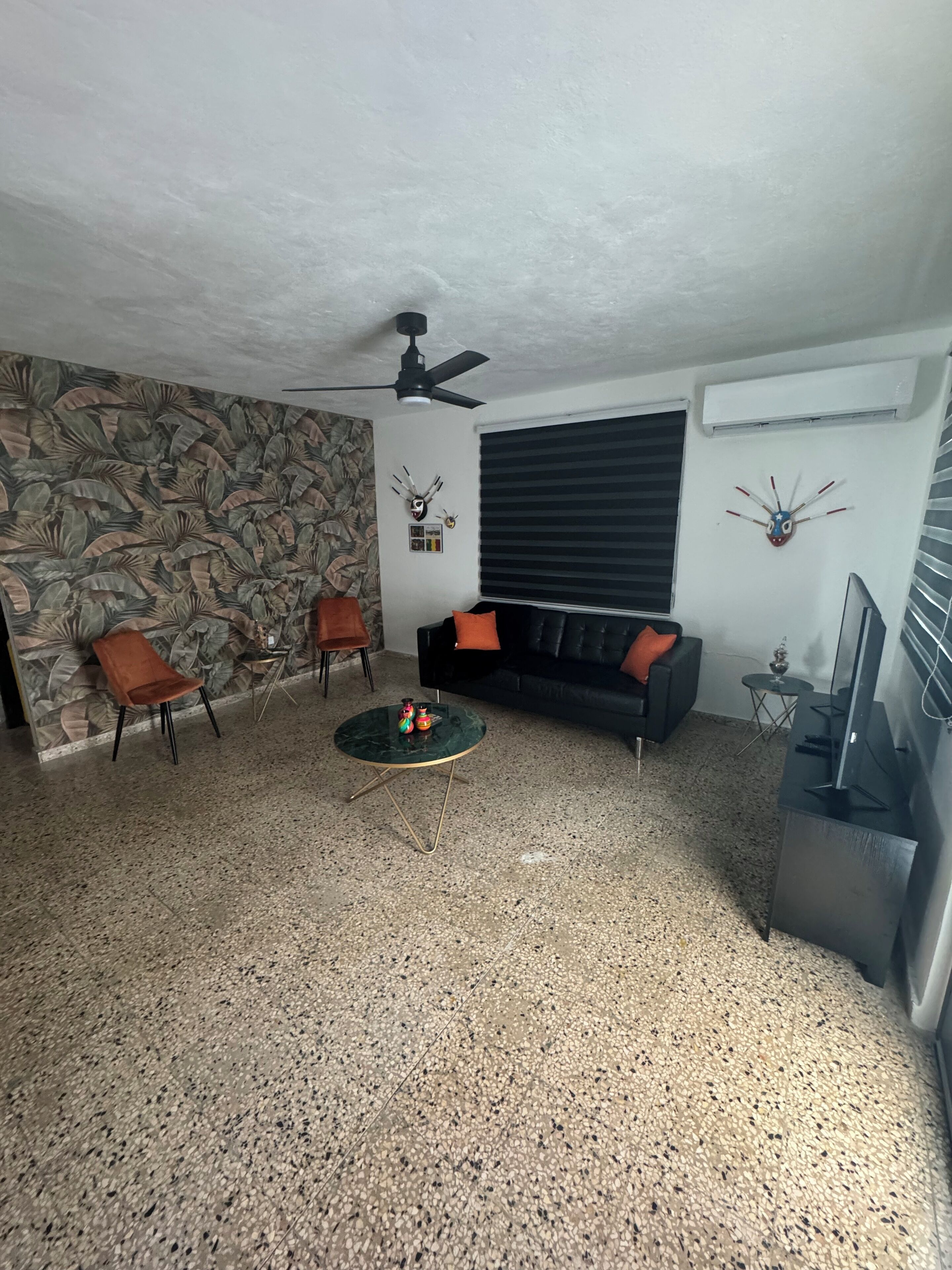 A living room with a sofa, two chairs, a coffee table, a ceiling fan, and decorative wall art.