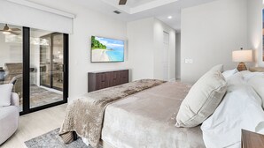 Une chambre dotée d’un grand lit, d’un ventilateur de plafond, d’un téléviseur fixé au mur et d’une porte-fenêtre coulissante donnant sur un balcon.