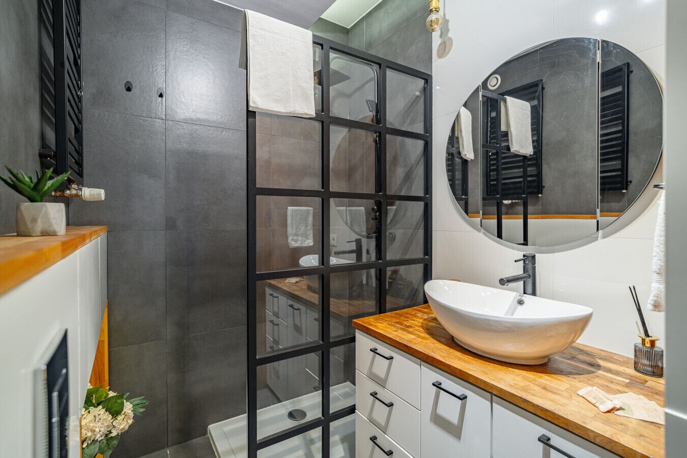 Une salle de bain moderne avec un grand miroir, un plan de travail en bois et un lavabo blanc.