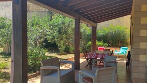Terrassa exterior amb mobles de vimet, una taula amb mantell estampat i una cadira vermella.