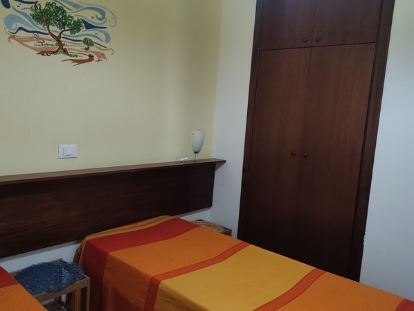 A room with two beds, a wooden wardrobe, a wall-mounted shelf with a vase, and a switchboard. - Villa Lucrezia – Relaxation, sea, and authentic Sicilian charm (Balestrate)