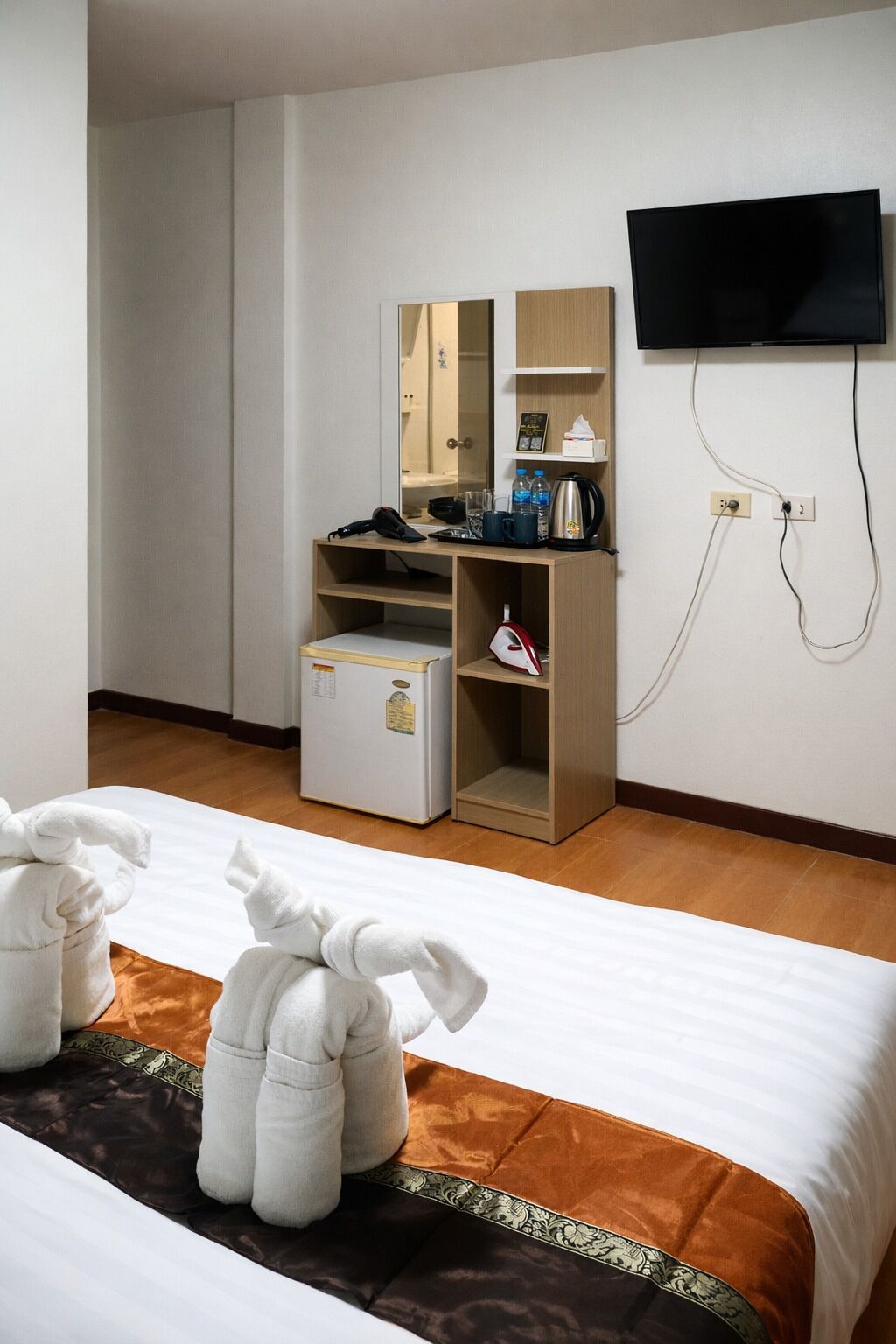 A hotel room with a bed, a desk with a mirror, a television mounted on the wall, and a minibar.