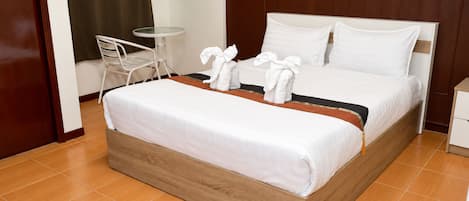 A hotel room with a bed, a small table, a chair, and a wall-mounted phone.