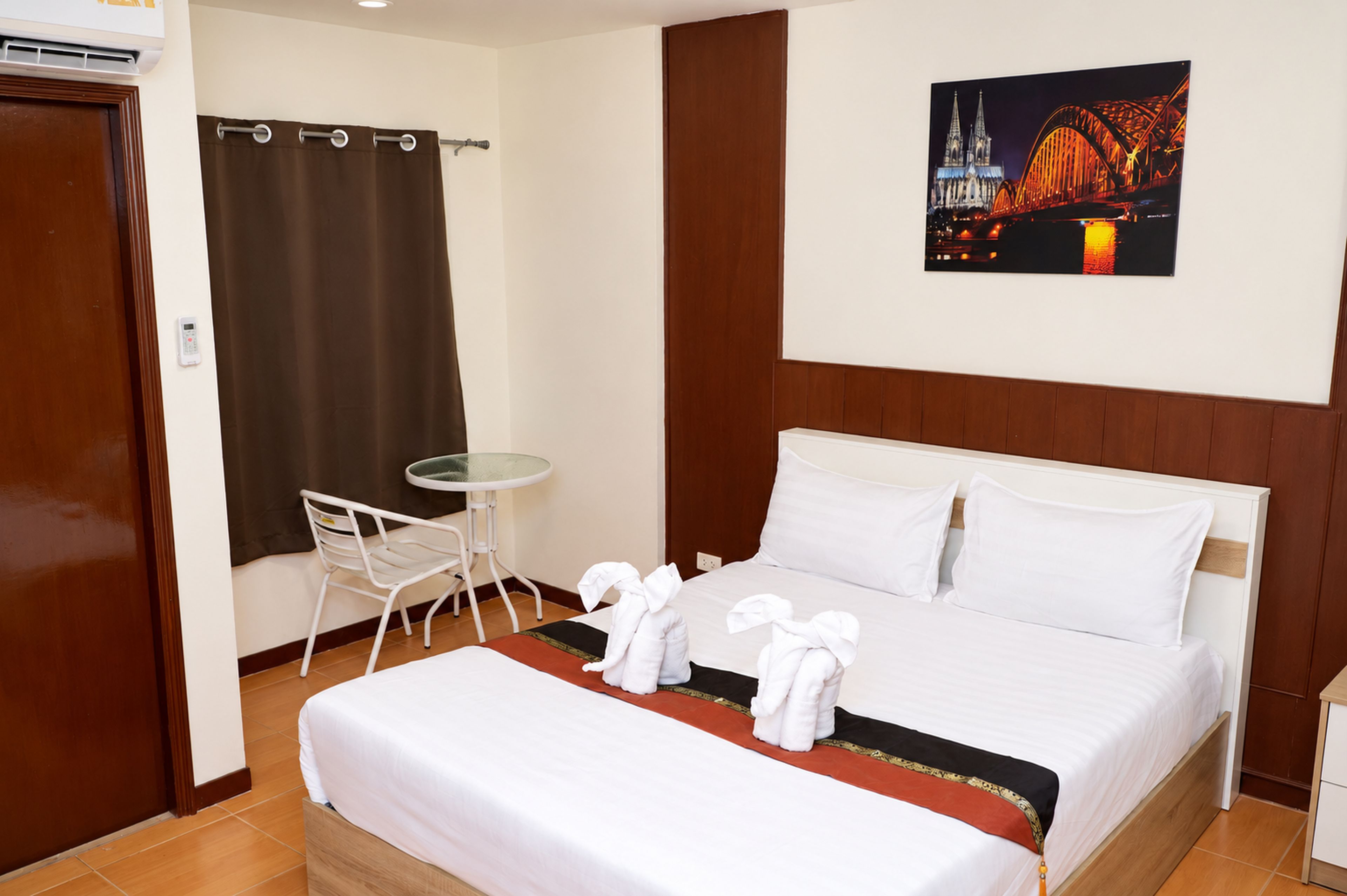 Habitación de hotel con cama, una mesita, una silla, cortina de ducha y un cuadro en la pared.