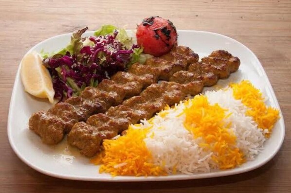 Une assiette contenant des brochettes, du riz, une salade et une tomate grillée.