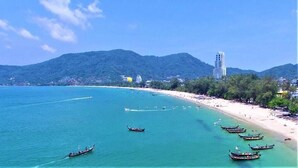A coastal scene with boats on calm waters, a beach, and a mountain in the background. - Azure Palace (Patong)