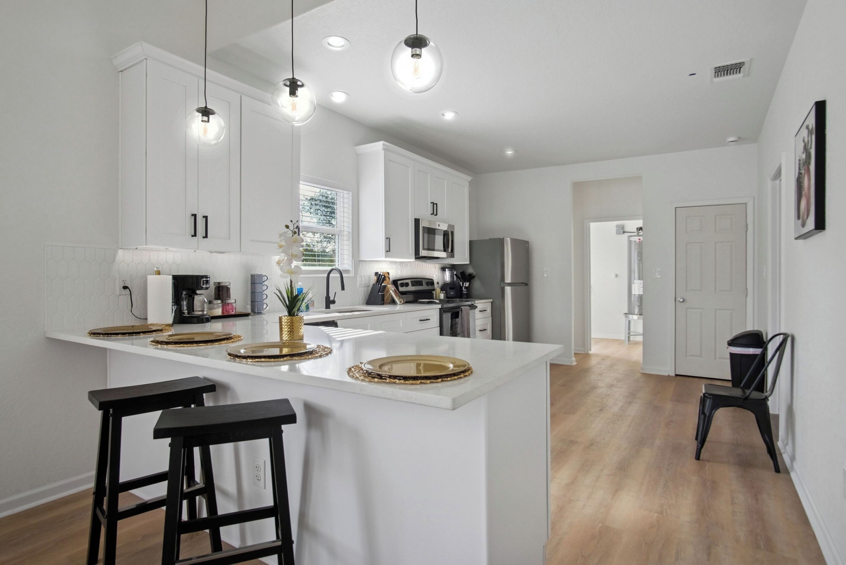 A modern kitchen with white cabinets, a central island with stools, and pendant lighting.