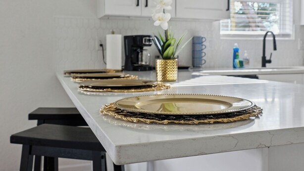 Una cocina con armarios blancos, encimera de mármol y platos con detalles dorados.