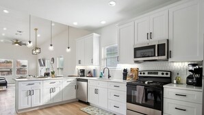 Una cocina moderna con armarios blancos, electrodomésticos de acero inoxidable e iluminación colgante.